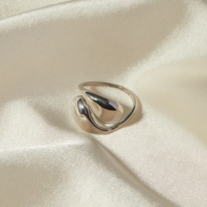 Detail of silver teardrop fluid ring on beige silk fabric with soft metallic reflections