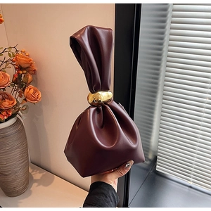 Detail of burgundy leather bucket bag with elegant knot design and golden metal ring hardware
