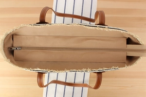 Detail view of woven straw tote bag featuring frayed tassel edges and secure zipper lining