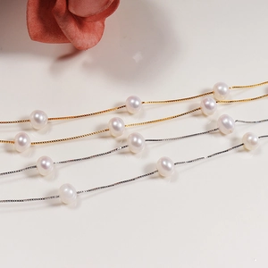 Macro detail of gold and silver box chains featuring white freshwater pearls in a close-up