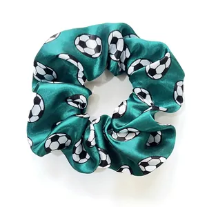 Close-up of green satin hair scrunchie featuring a repeating black and white soccer pattern