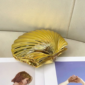 Detailed macro view of the shell-shaped evening clutch with gold metallic mirror texture