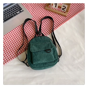 Flat lay of a dark green corduroy mini backpack featuring a front pocket and D-ring detail