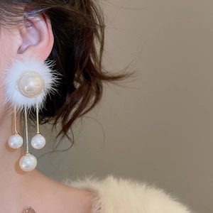 Detail of elegant earrings with white pom-poms, pearls, and tassels worn by a model