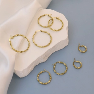 Detailed view of three sizes of gold-plated twisted hoop earrings on stone display
