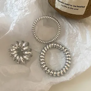 Three pieces of metallic silver spiral telephone wire hair ties on white paper background