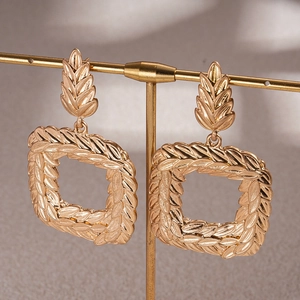 Macro detail of gold square drop earrings featuring intricate wheat ear embossed textures