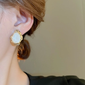 Close-up of vintage irregular gold earrings with cream stone inlay on model's ear