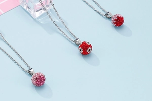 Three silver-plated necklaces with red and pink rhinestone clay ball pendants on blue surface