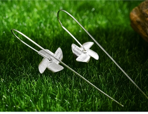 Detail of S925 sterling silver windmill earrings placed on fresh green grass