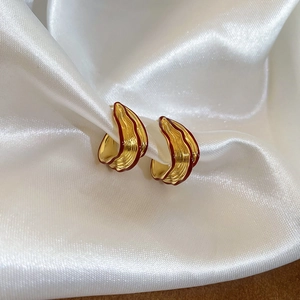 Macro shot of gold shell earrings with red enamel edges on white silk fabric