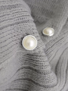Macro detail of decorative pearl buttons with silver texture on grey knit sweater