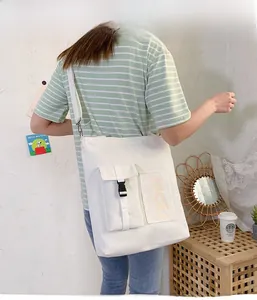 Detail view of white canvas tote bag featuring front buckle pocket and adjustable strap