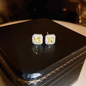 Macro shot of square yellow zircon earrings with halo diamond setting on black jewelry box
