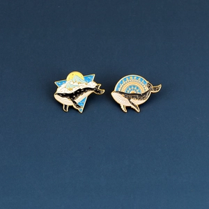 Detail view of two enamel whale pins featuring Mount Fuji and celestial patterns
