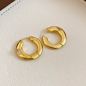 Detailed close-up of gold plated chunky hoop earring with white zircon on leather