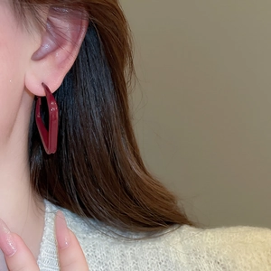 Close-up of a woman wearing deep red geometric diamond-shaped glossy earrings