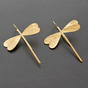Macro detail of golden dragonfly earrings with textured hammered finish wings