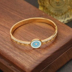 Close-up of golden evil eye bangle with blue enamel and pavé rhinestones on wood