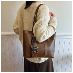 Detail of brown leather tote bag with white contrast stitching and cat charm accessory