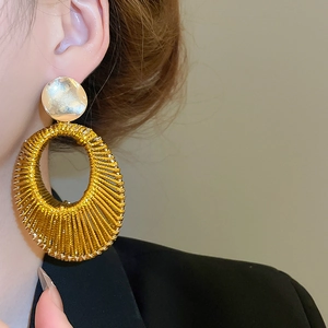 Gros plan de boucles d'oreilles pendantes ovales tissées dorées portées par un mannequin