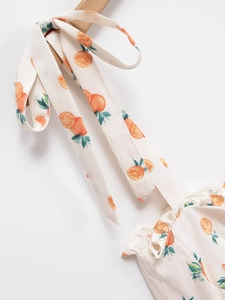 Vue détaillée de l'imprimé orange sur tissu blanc montrant le nœud papillon de la robe