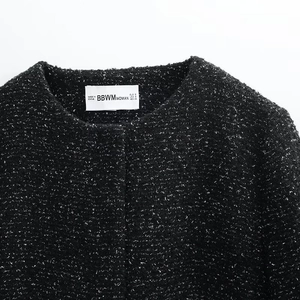 Detail of black tweed jacket neckline with woven texture and white sizing label