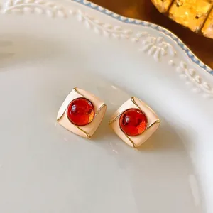 Vintage square earrings with cream enamel border and deep red gemstone in ceramic dish