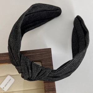 Close-up of the knotted black denim headband texture on a wooden display stand
