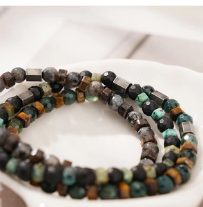 Macro shot of faceted tiger eye and obsidian beaded bracelets on a white ceramic tray