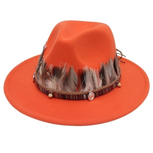 Detail eines orangen Wollhutes mit Federn, gewebtem Band und Ethno-Metallanhängern