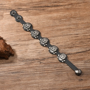 Detail of black leather bracelet with five silver skull and crossbones on wooden surface