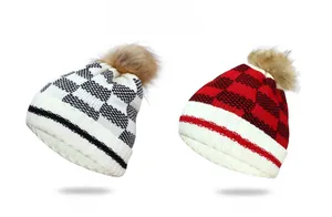 Detail view of thick knitted beanies with fluffy faux fur pom-poms in black and red plaid