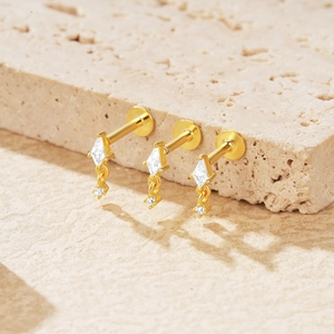 Detail of three gold floral earrings with clear zircons on a textured stone surface