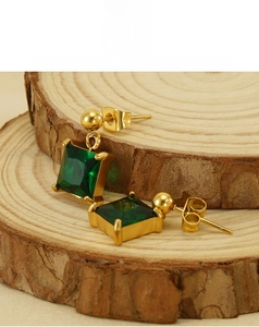 Detail of 18K gold-plated earrings with emerald-cut green zircon on a wood stand