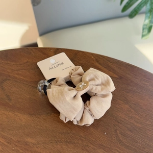 Detail of beige cotton linen hair scrunchie with oval bow tag on a wooden surface