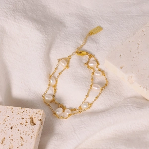 Double-layered gold chain bracelet featuring natural white pearls on white fabric background