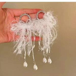 Detail view of silver earrings featuring white feather tassels and pearl drop pendants