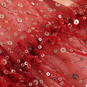 Detailed macro view of luxury red mesh fabric with shimmering gold sequins and pleats