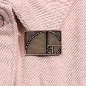 Macro detail of vintage golden ratio spiral metal brooch pinned on pink denim fabric