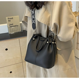 Detail of black lychee texture bucket bag with geometric wide shoulder strap and gold hardware