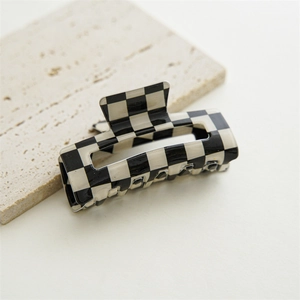 Macro detail of high-gloss black and white checkerboard hair claw clip on stone surface