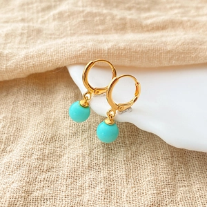 Macro view of gold hoop earrings with turquoise beads hanging on a ceramic bowl edge