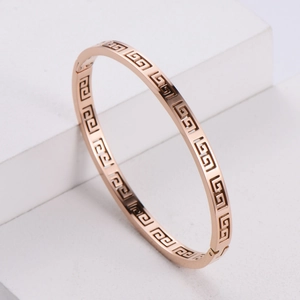 Rose gold stainless steel bangle with cutout geometric pattern on a white pedestal