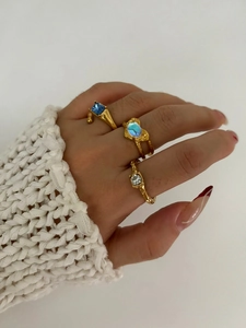Detailed view of irregular gold rings with heart opal and blue gems on hand