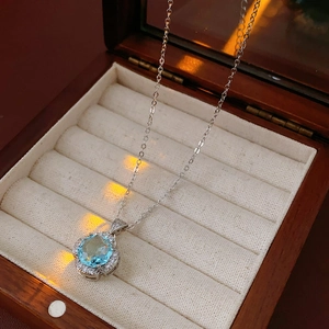 Macro shot of blue zircon flower pendant on beige velvet within a luxury wooden jewelry box