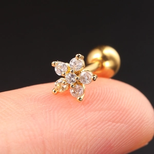Macro view of a gold flower earring with clear cubic zirconia held on a fingertip