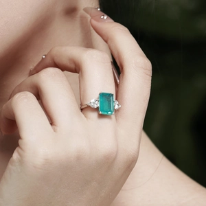 Close-up of an emerald-cut green gemstone ring with diamonds on model's finger