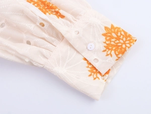 Dettaglio del polsino ricamato con stampe floreali arancioni e chiusura con bottone bianco