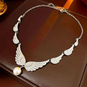 Macro detail of silver wing necklace featuring sparkling crystals and a central pearl pendant
